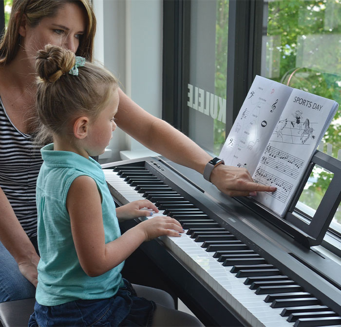 girl in blue and teacher working at piano